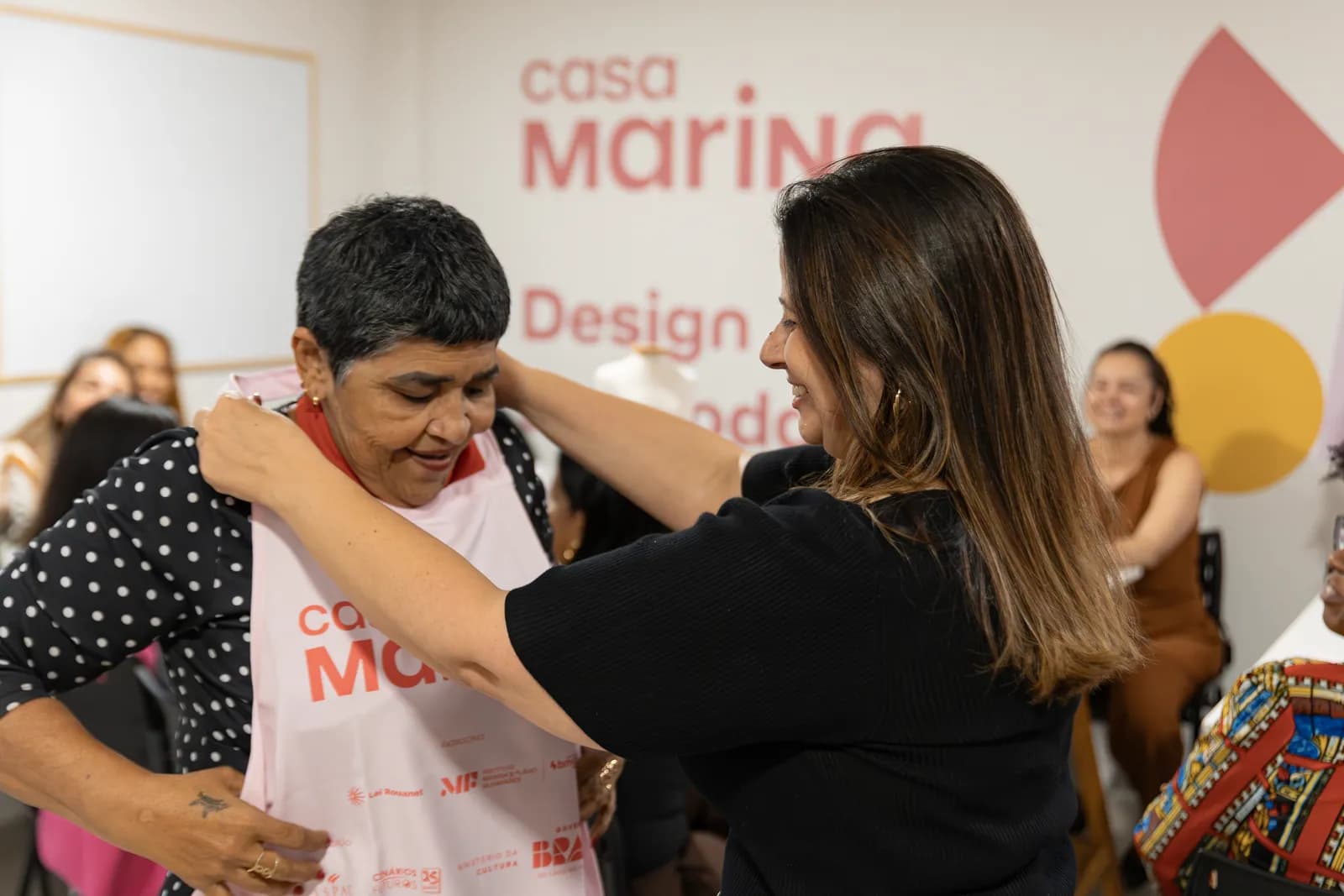Professora ajudando aluna a vestir o avental da Casa Marina